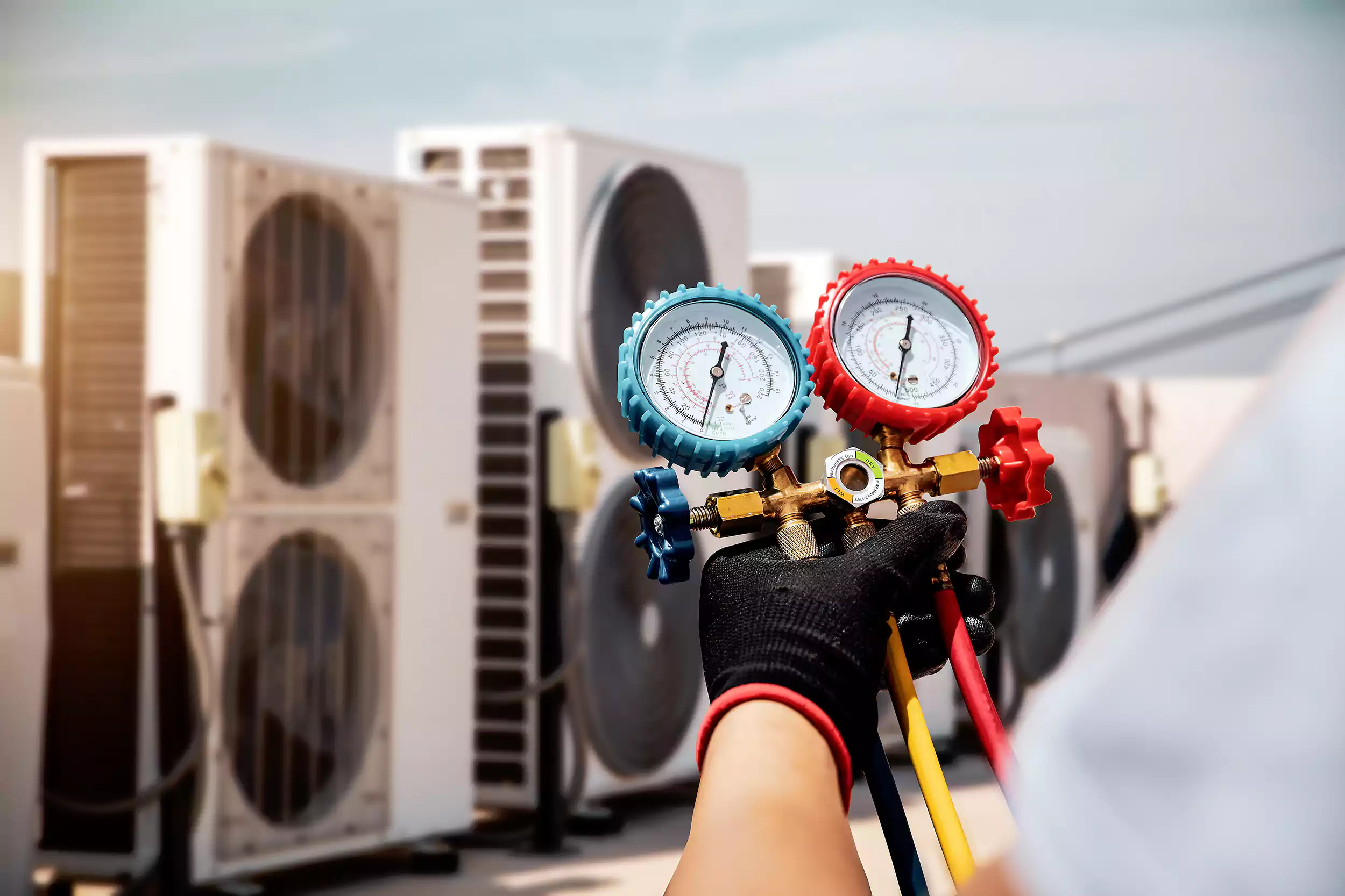 Technician using refrigerant manifold gauges on outdoor HVAC condenser units