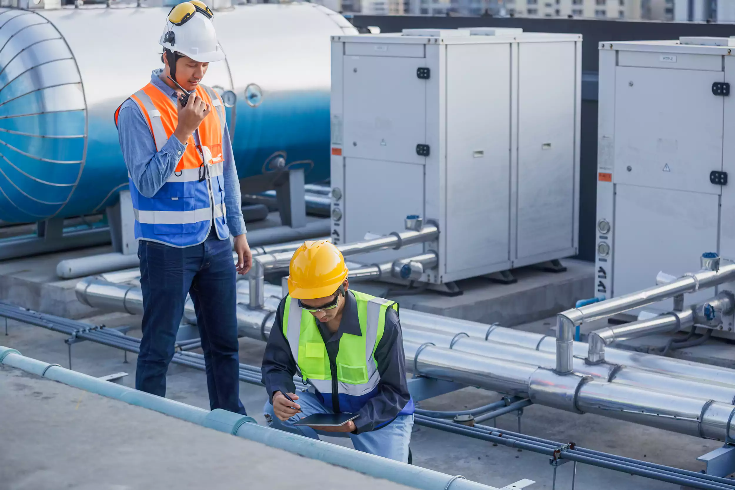 Two engineers in high-visibility vests inspecting rooftop mechanical plant on a commercial building