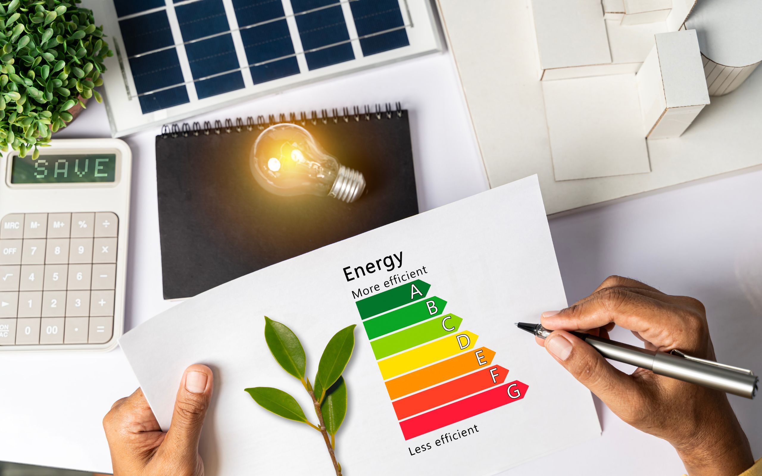 An energy efficiency rating chart from A to G being reviewed on a desk beside a solar panel, a calculator and a building model